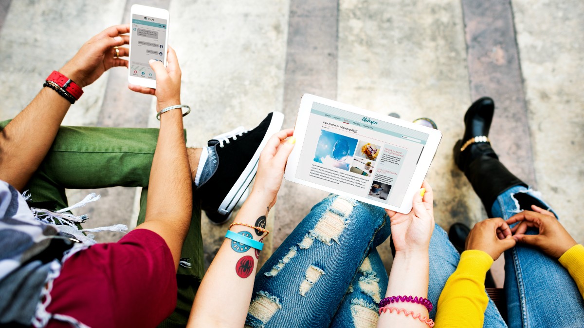 Jóvenes consultan noticias en dispositivos digitales.