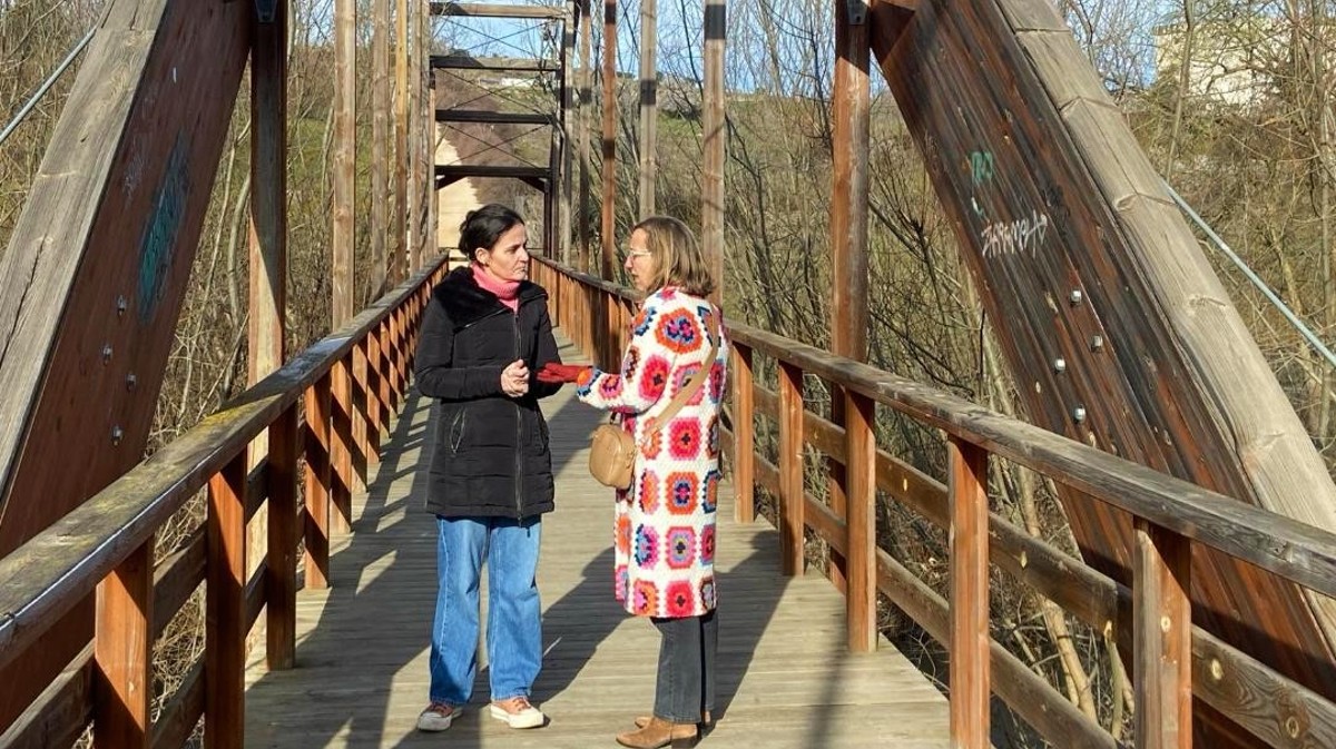 La teniente de alcalde y una técnica municipal en el puente de madera sobre el río Adaja.