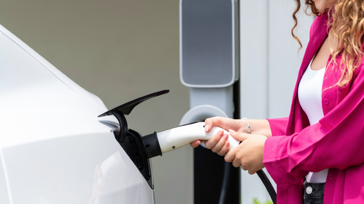 Una mujer recarga un veh&iacute;culo el&eacute;ctrico.