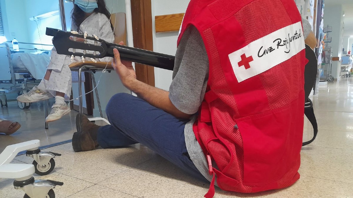 Un voluntario de Cruz Roja toca la guitarra ante un ni&ntilde;o en el hospital.