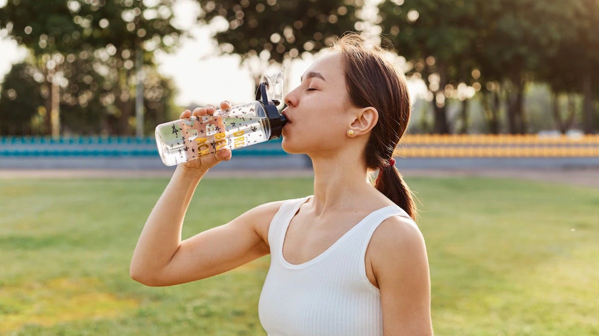 Una deportista bebe agua bajo el calor.
