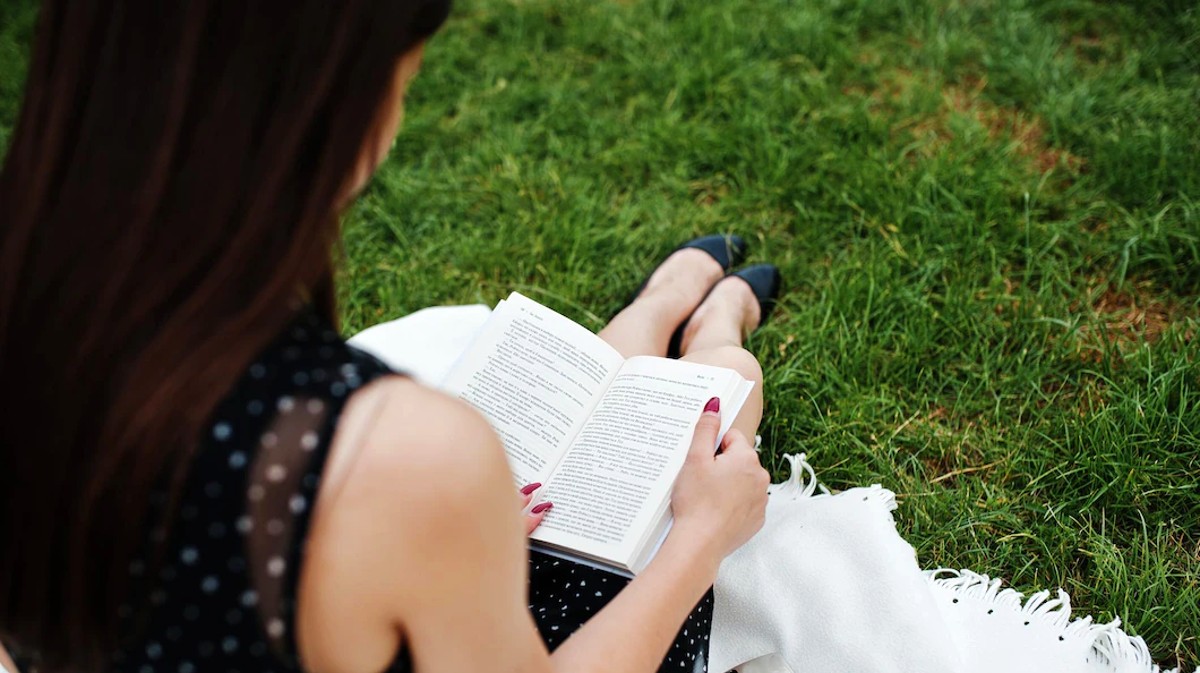 Una joven lee en un jardín.