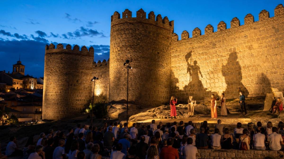Actores representan una escena frente a la muralla iluminada mientras el p&uacute;blico observa sentado