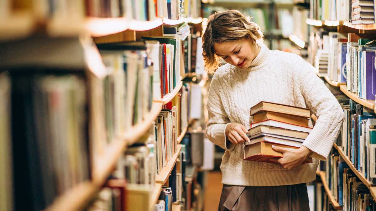 Una mujer recoge libros en una biblioteca.